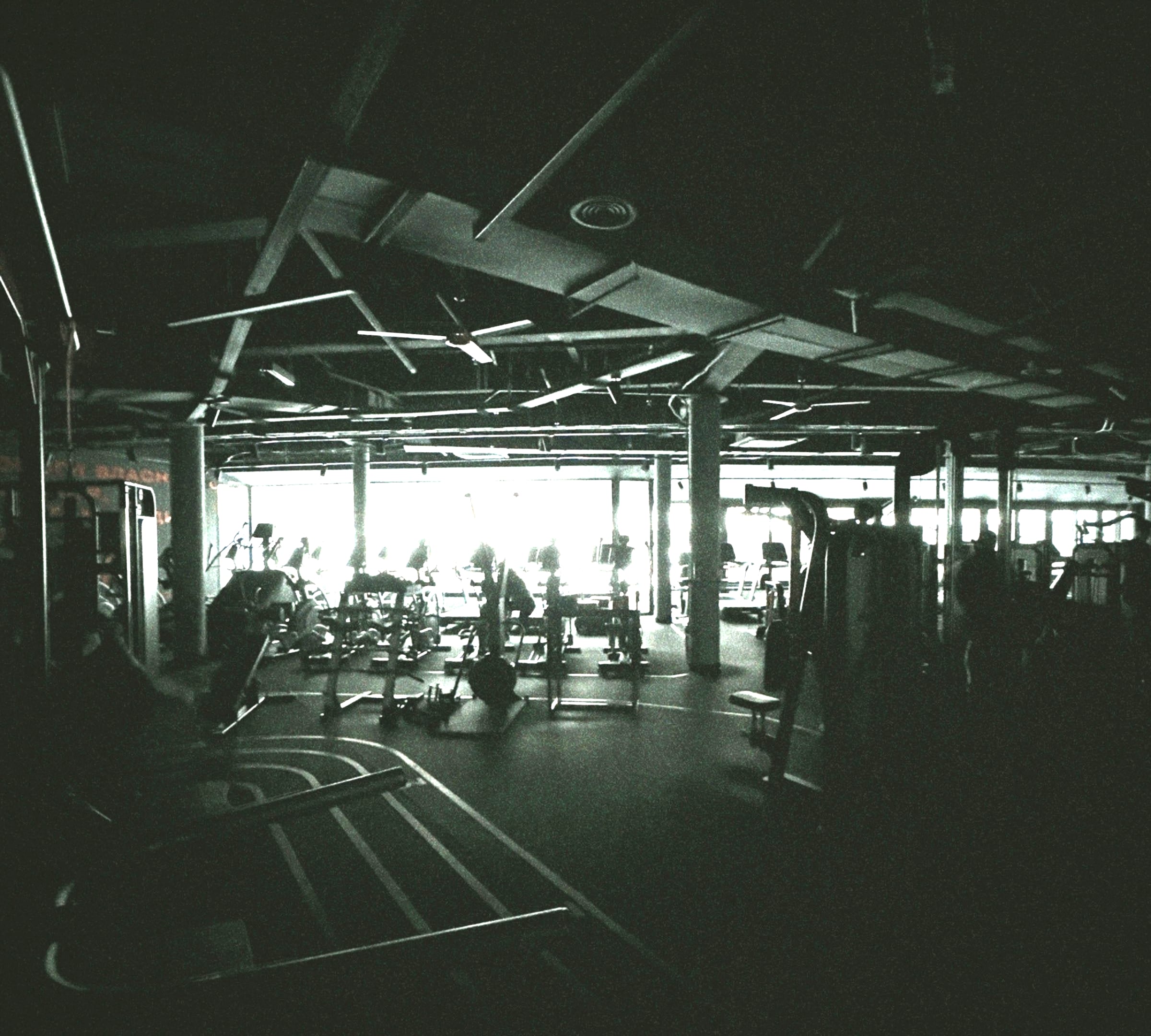 Gym floor in low light, with rows of machines in front of tall windows.