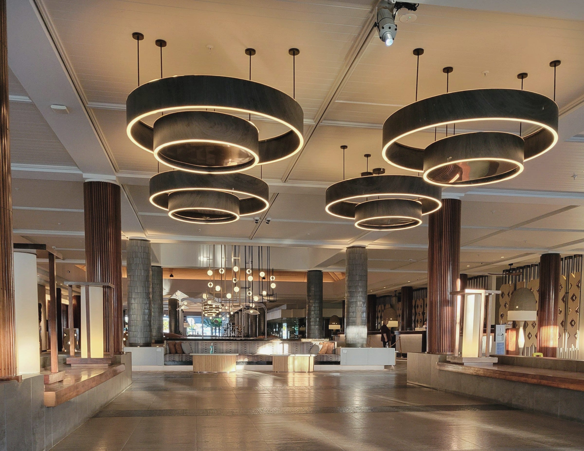 Hotel lobby in the evening, with large ring-shaped pendant lights glowing above a quiet seating area.