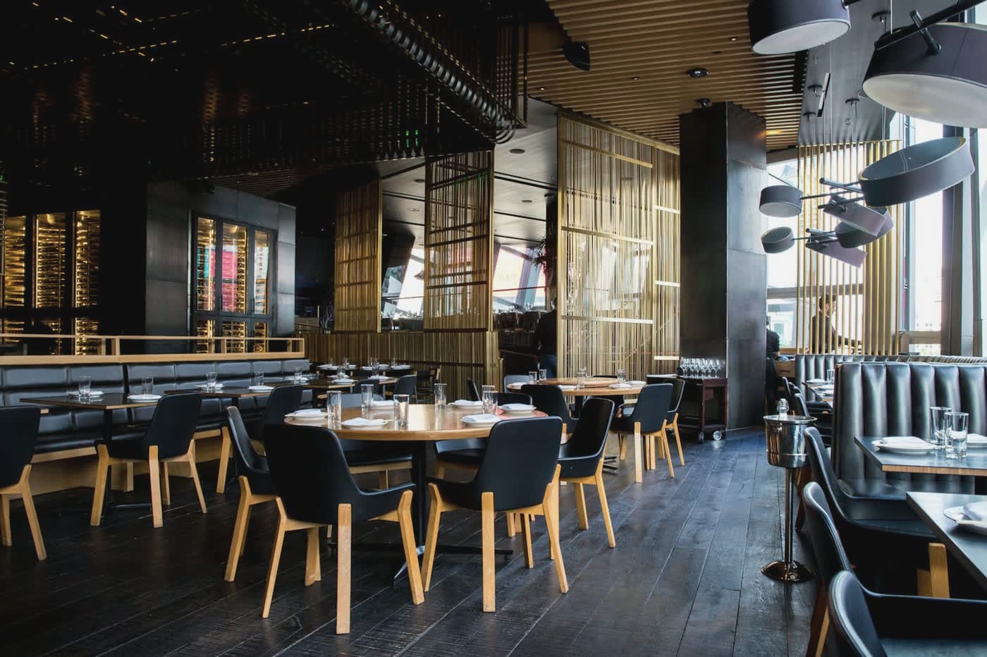 Empty restaurant dining room with dark wood floors, set tables and amber chairs under low pendant lamps.